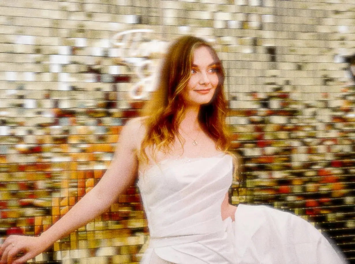 A bride in a white gown in front of a gold sequin backdrop