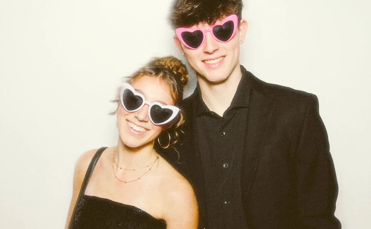 A couple in black with heart sunglasses posing at the photo booth