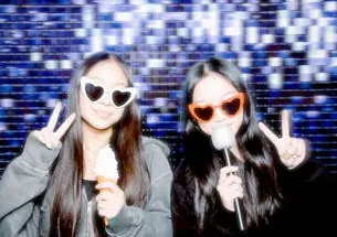 Two young women posing with microphones in front of the photo booth