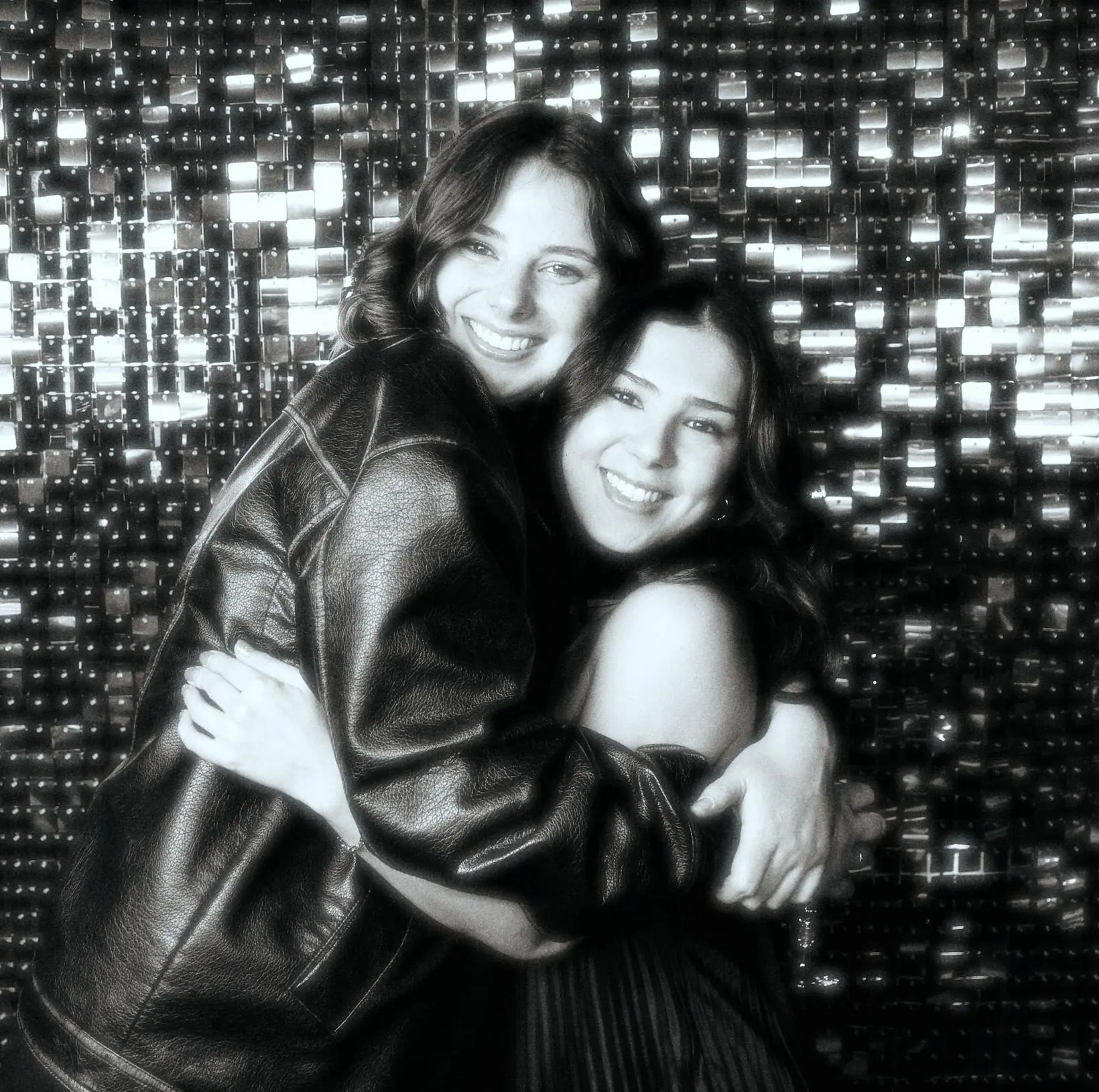 Two wedding guests hugging in front of a sequin backdrop, in black and white