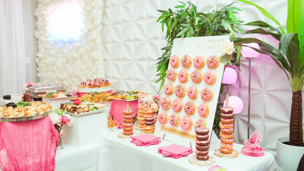 Viva donut wall with pink sprinkled donuts and donut towers on a white dessert table