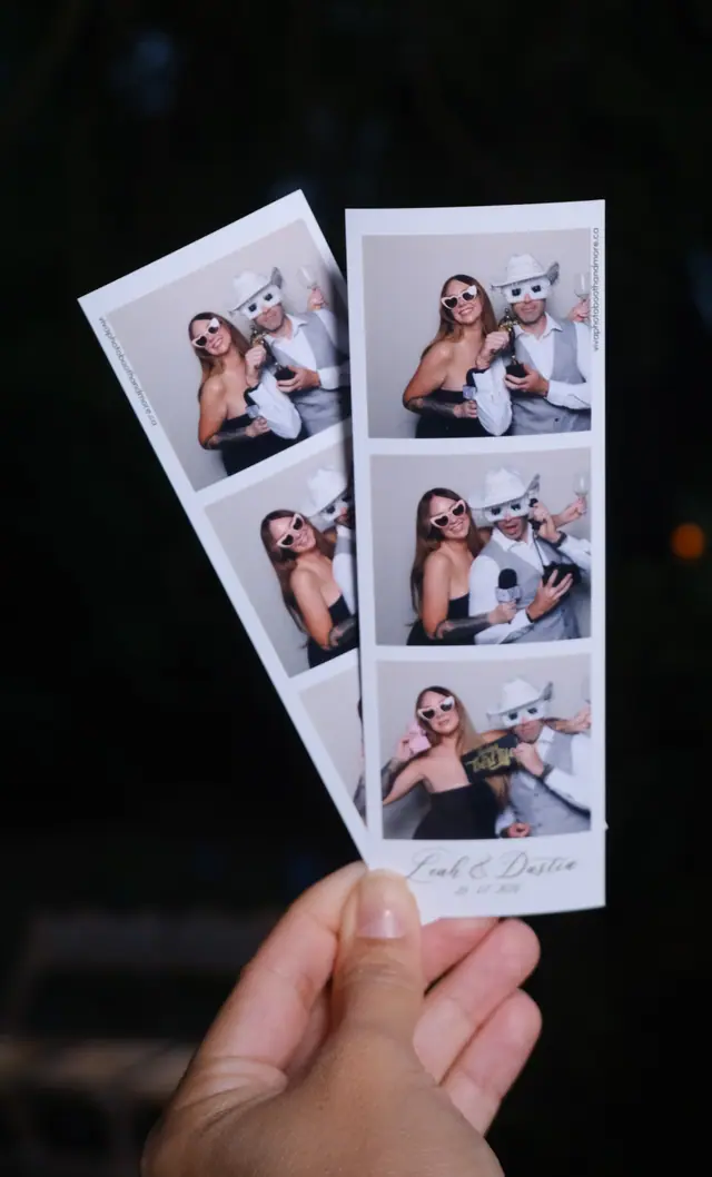 A hand holding two printed photo strips from a wedding, personalised with the couple's names