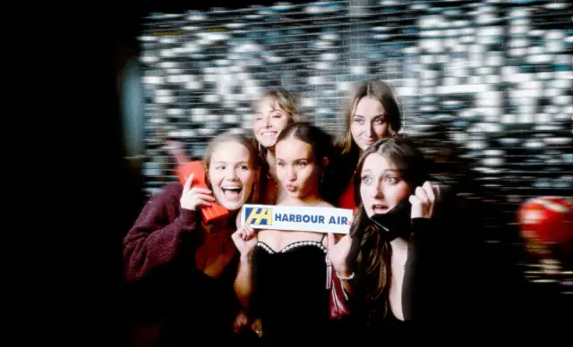 Group of friends holding a Harbour Air sign at a sequin backdrop