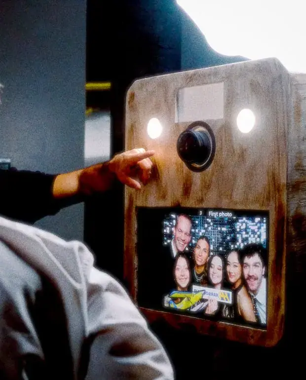Guest pressing the button on the wooden Viva booth, the photo preview on its screen