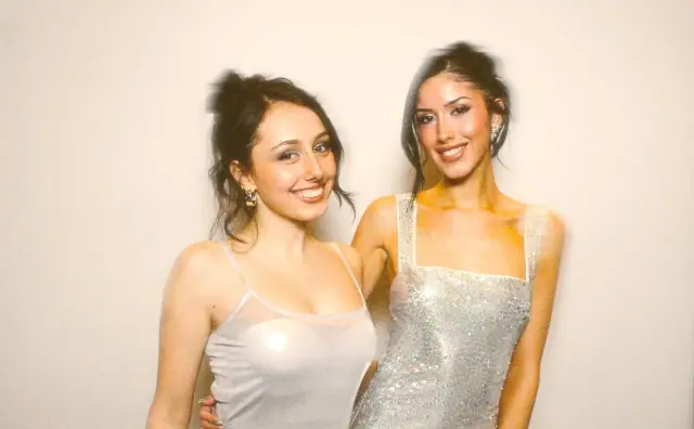 Two women in party dresses posing on a white photo booth backdrop