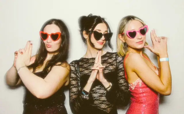 Three friends posing with heart sunglasses on a white backdrop