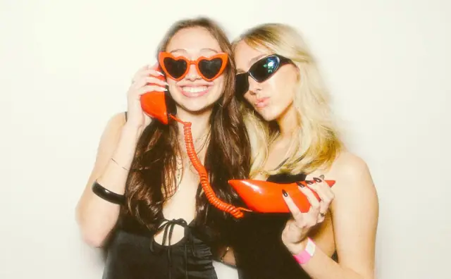 Two friends with a red telephone prop and heart sunglasses