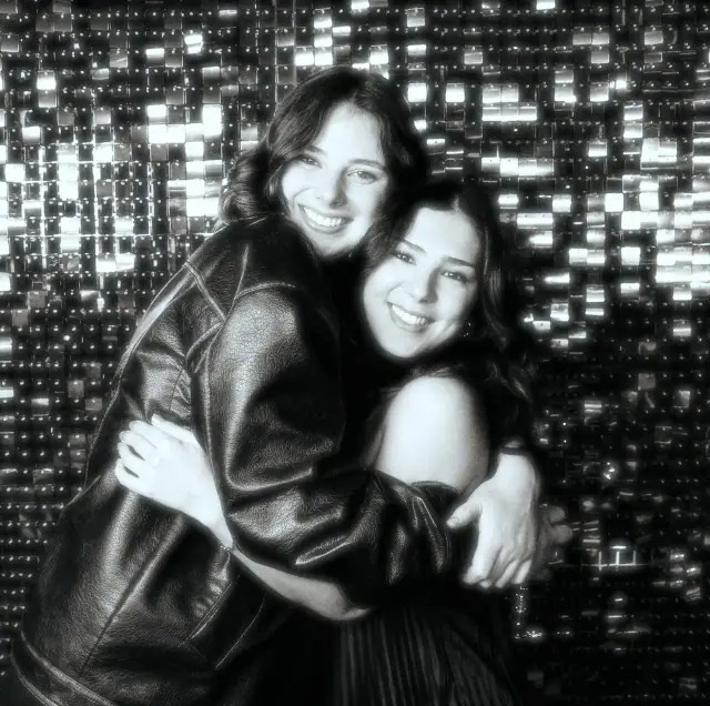 Two friends hugging in front of a sequin wall, black and white booth photo