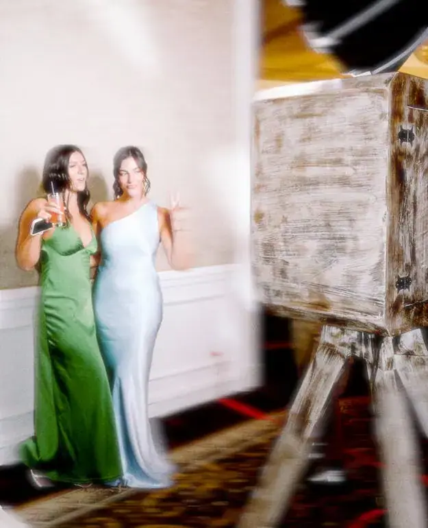 Two guests in green and blue gowns beside the wooden open-air booth