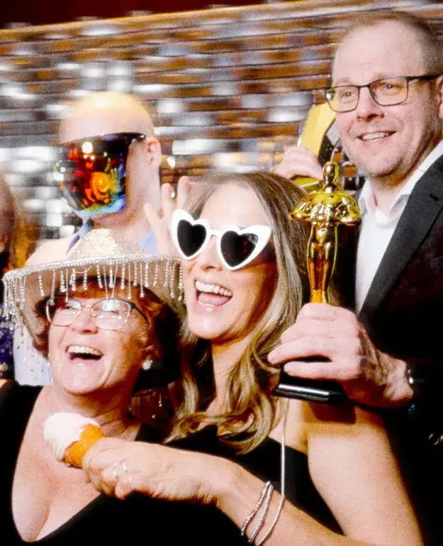 Laughing guests with heart sunglasses, a sequin hat and a trophy prop