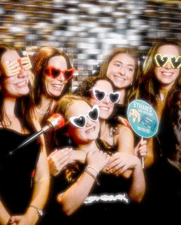 Group of friends in heart sunglasses holding props in front of a sequin backdrop