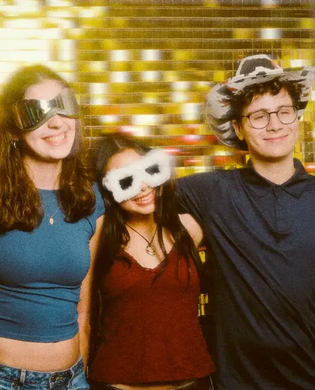 Three friends in goggles, a fluffy mask and a cowboy hat on a gold sequin backdrop